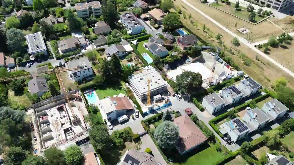 Vue aérienne d'un quartier résidentiel genevois, deux chantiers avec grues en cours parmi les villas